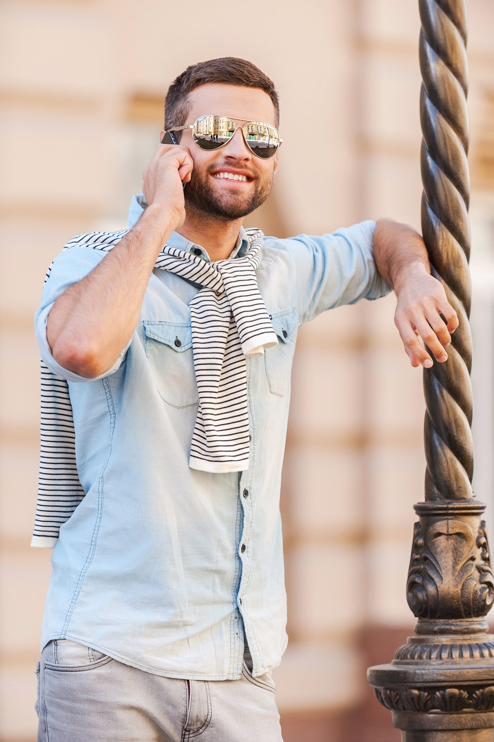 Young hipster talking on the phone leaning against a pole